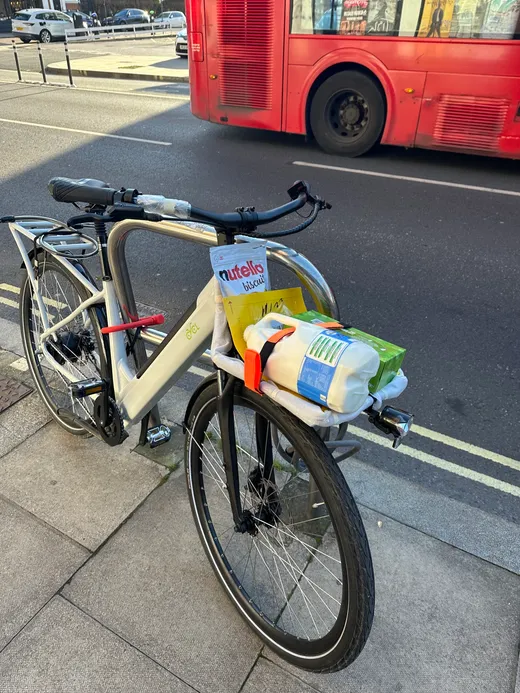 Groceries strapped to the front rack of an electric cargo bike, London bus behind
